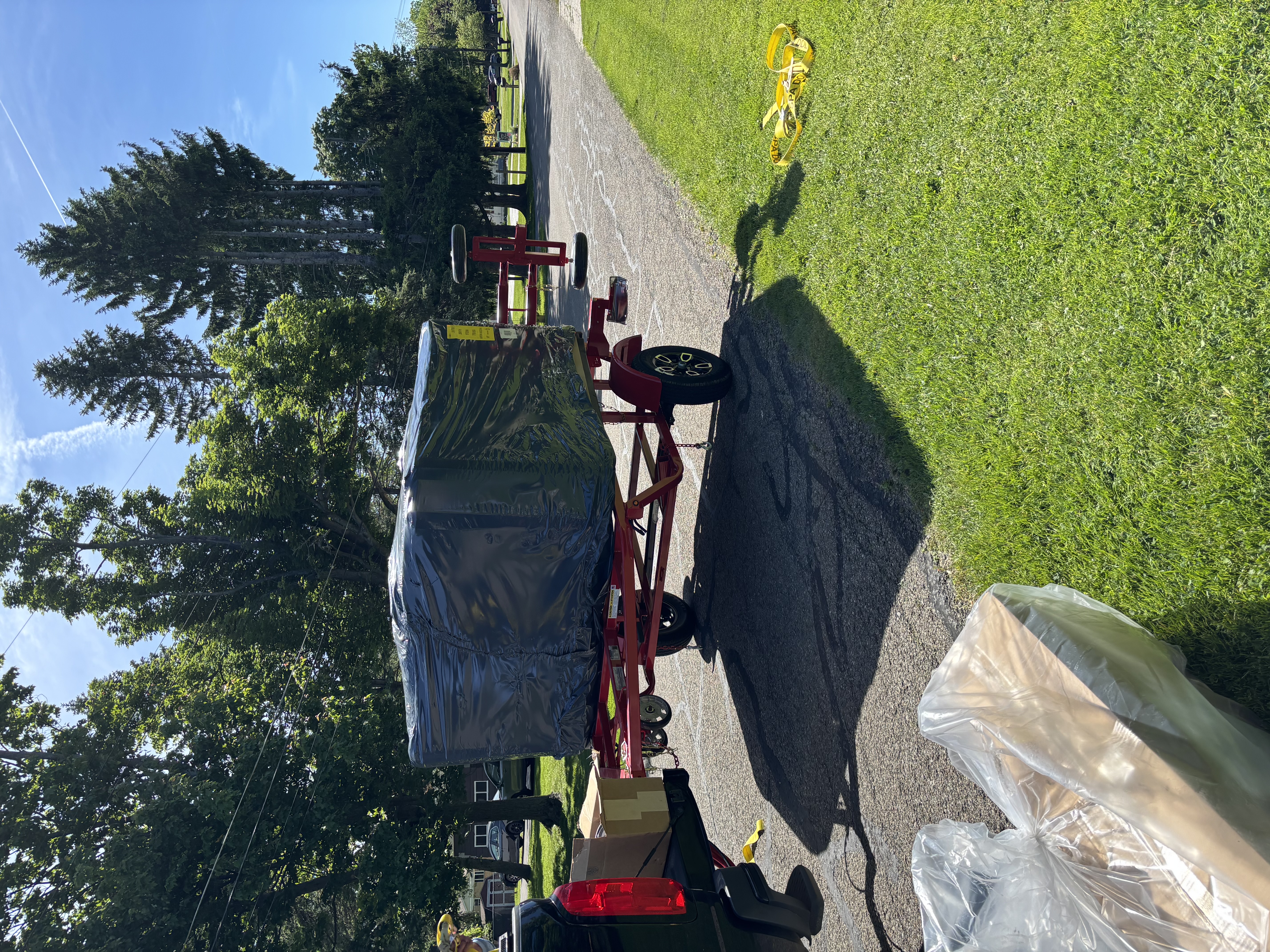 Wrapped spa secured on a red trailer behind a pickup truck on a neighborhood street